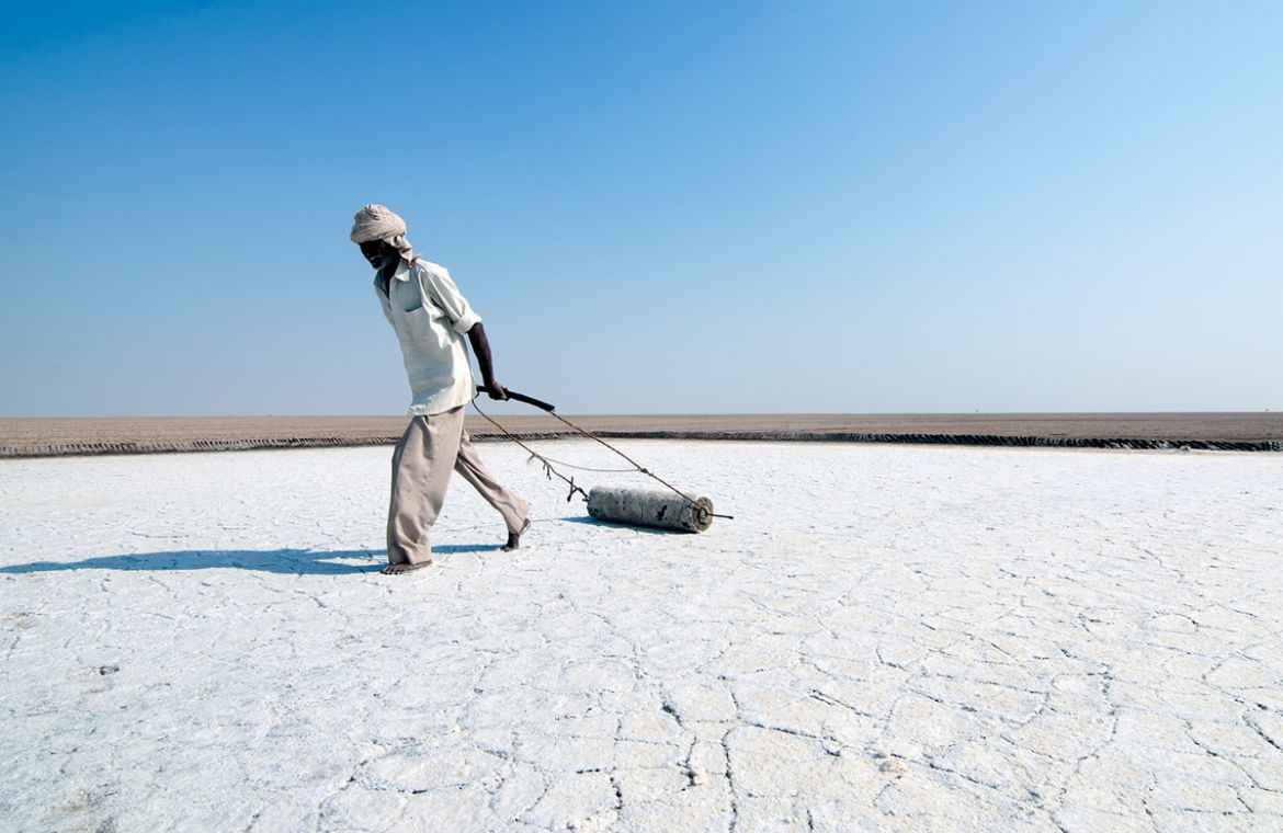 Davalram, 64, leveling the salt pan his family has worked on for generations. Most of his friends who started salt farming with him half a century ago, have died. [Sugato Mukherjee/Al Jazeera]