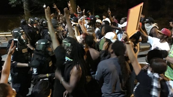 Protestors demonstrate in front of police officers wearing riot gear in Charlotte