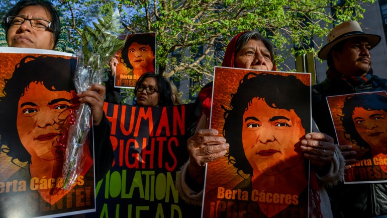 Protesters hold placards with photos of Berta Caceres and banners denouncing human rights abuses.