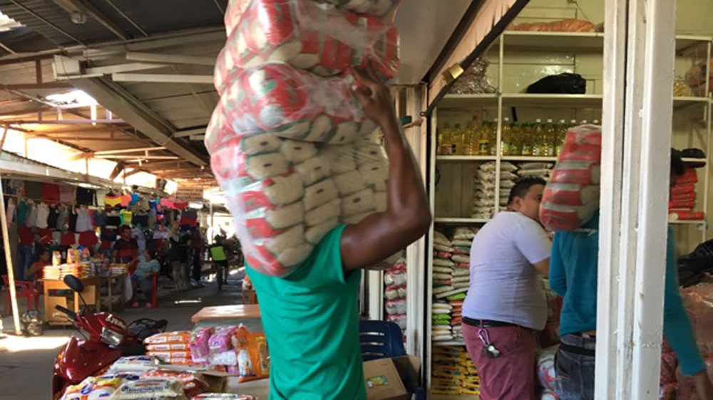 A man carries a heavy load of flour into a Puerto Santander store where Venezuelans cross the border to shop [Anne Bouleanu/Al Jazeera] 