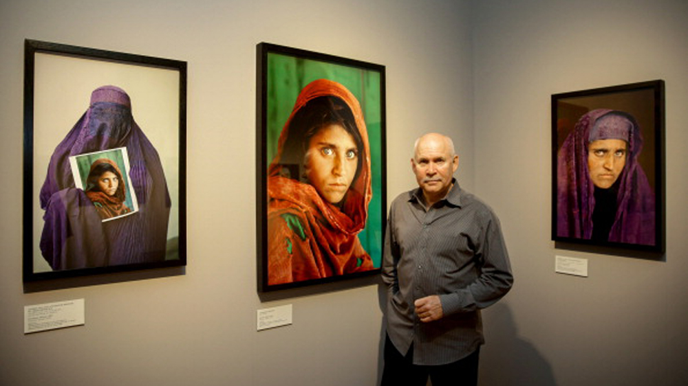 US photographer Steve McCurry poses next to his photos of the 'Afghan Girl' Sharbat Gula in Hamburg in 2013 [Ulrich Perrey/AFP/Getty Images]