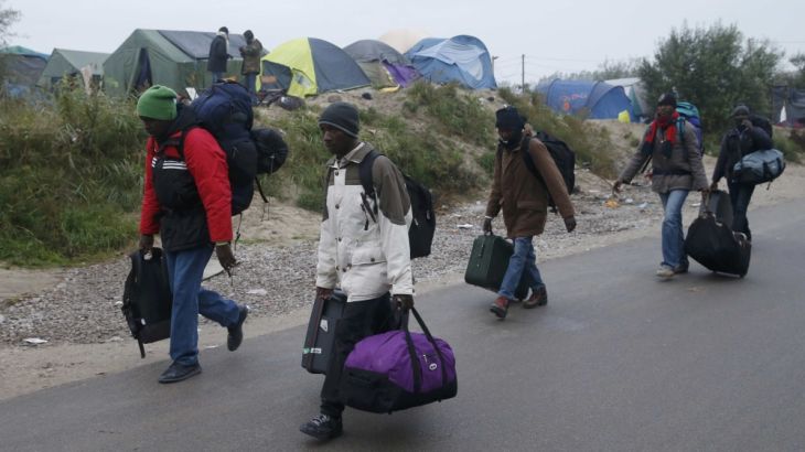 Migrants with their belongings walk past tents at the start of the"Jungle" in Calais