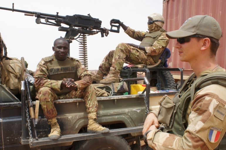 French and Malian soldiers wait for an armored car to be dug out of sand in Inat