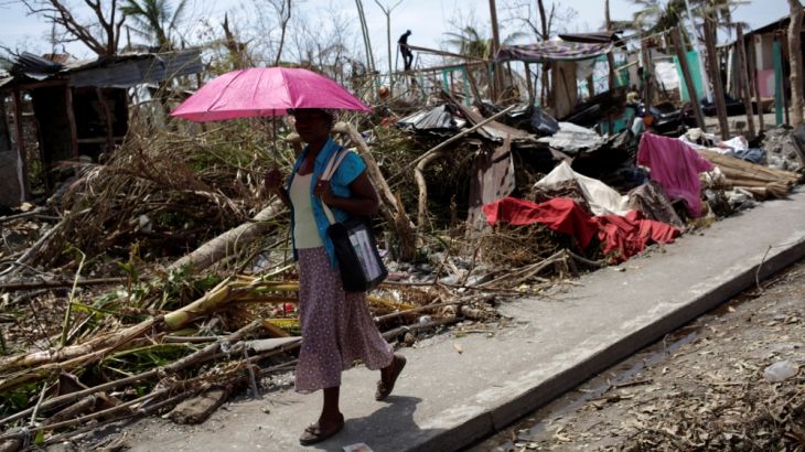 A woman holds an umbrella as she walks next to houses destroyed by Hurricane Matthew in Les Anglais, Haiti