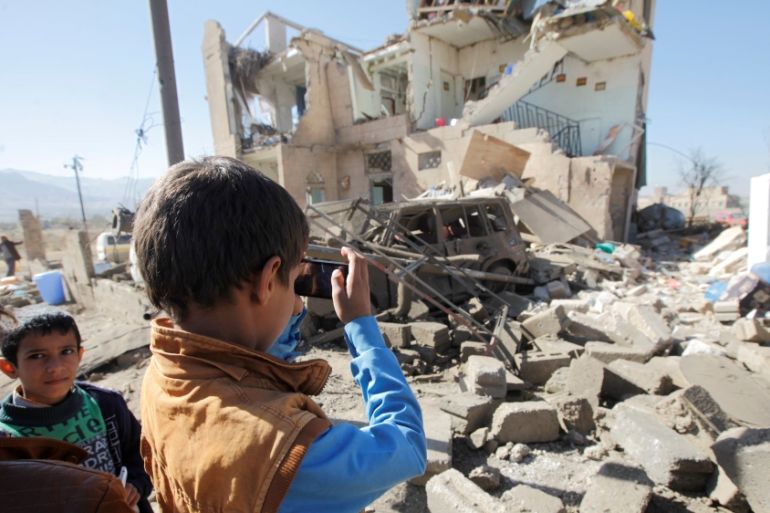 A boy uses a cell phone to take photos of the wreckage of a house destroyed by a Saudi-led air strike on the outskirts of Sanaa