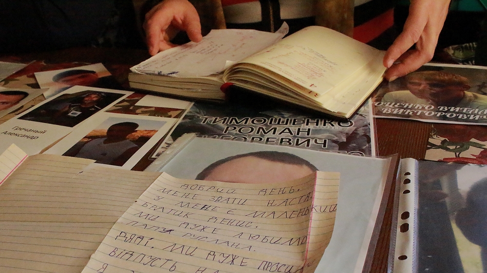 Olena Sugak spreads photos of missing Ukrainians across the table. A handwritten letter by Sugak's grandchildren, Nastia and Dennis, plead for the return of their father, who is currently missing in East Ukraine [Matthew Vickery/Al Jazeera]
