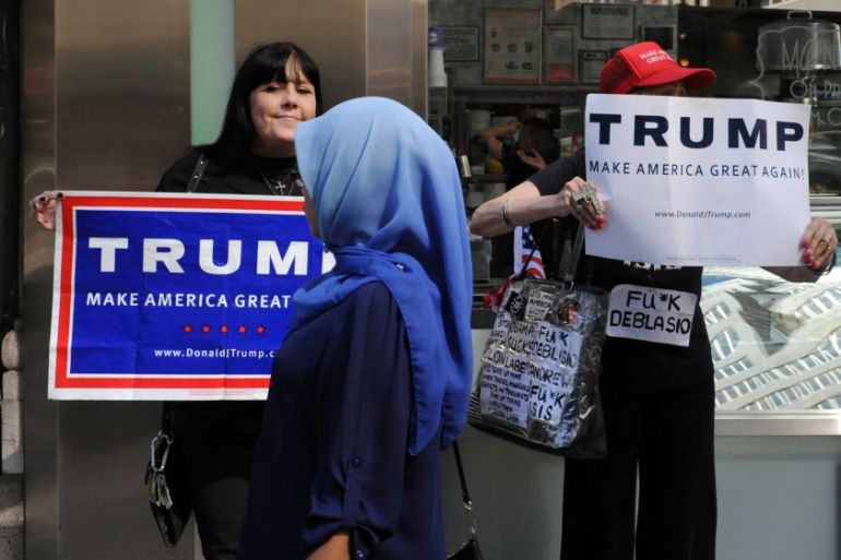 A woman wearing a Muslim headscarf walks past people holding U.S. Republican presidential nominee Donald Trump signs before the annual Muslim Day Parade in the Manhattan borough of New York City