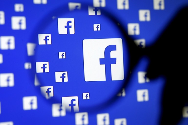 A man poses with a magnifier in front of a Facebook logo on display in this illustration taken in Sarajevo