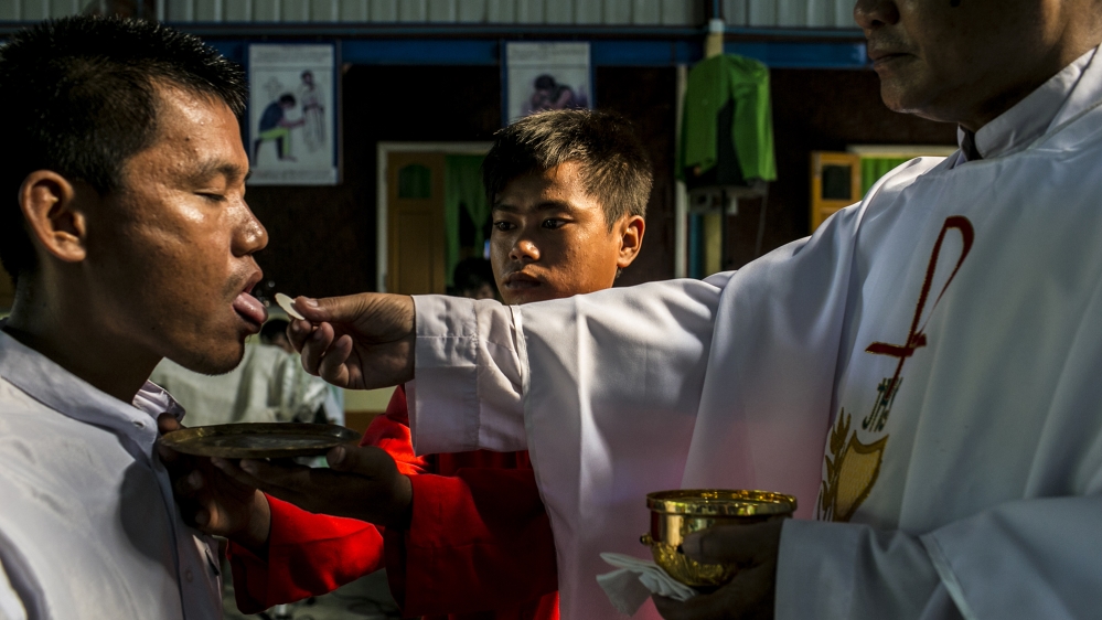 Bawn Hkaw, 23, another client of the Rebirth Rehabilitation Centre, helps a Catholic priest give mass to Columban Htung La, 38, another ex-drug user of the centre [David Shaw/Al Jazeera]