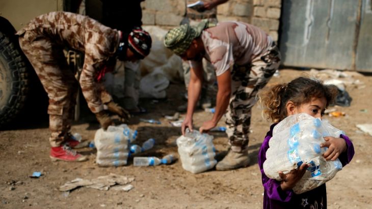 A girl carries bottles of water given by Iraqi soldiers in a village outside Mosul