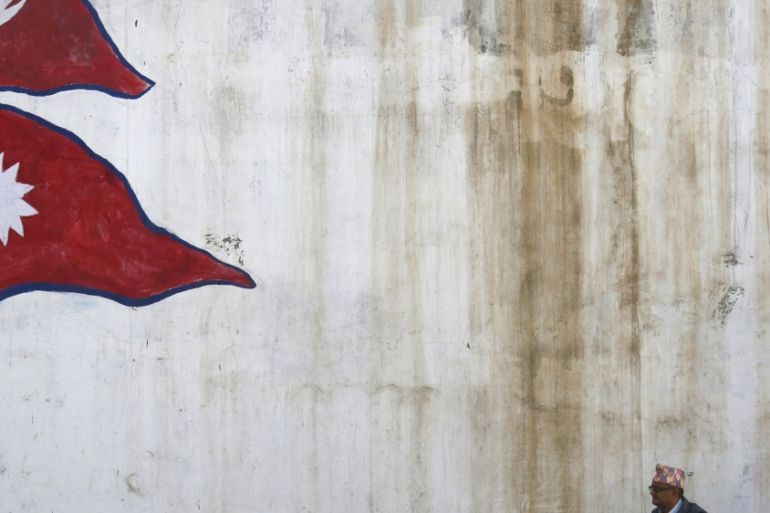 Man stands near a wall with a painting of a Nepali national flag as he waits for a bus in Kathmandu, Nepal