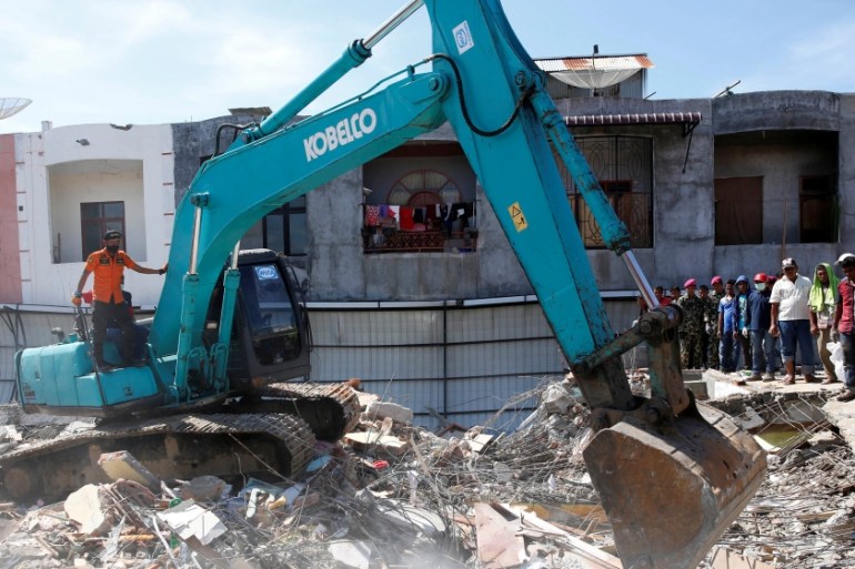 Rescue teams use heavy equipment to dig through a collapsed building following a strong earthquake in Meureudu market, Pidie Jaya