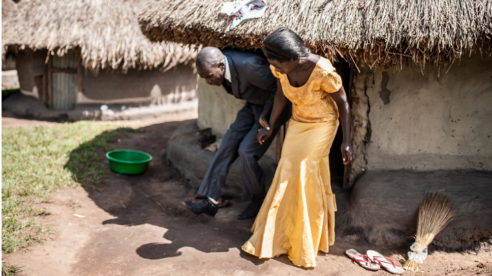Simon Peter Otoyo's wife, Atino Marie, assists him in leaving their home in Western Uganda. Although he has become very independent, Otoyo still relies on the help of his family [Aurelie Marrier d'Unienville/Sightsavers/Al Jazeera]