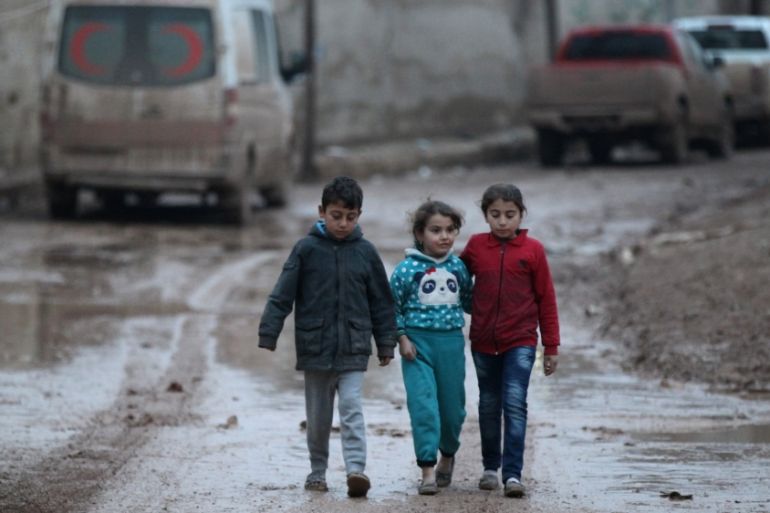 Children walk near a parked ambulance vehicle in al-Rai town, Aleppo
