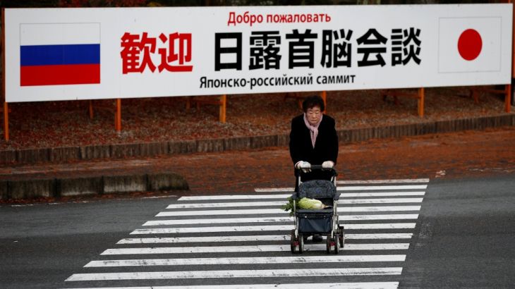 A woman walks in front of a sign board that reads "Welcome Japan Russia summit meeting" near a hot spring resort in Nagato