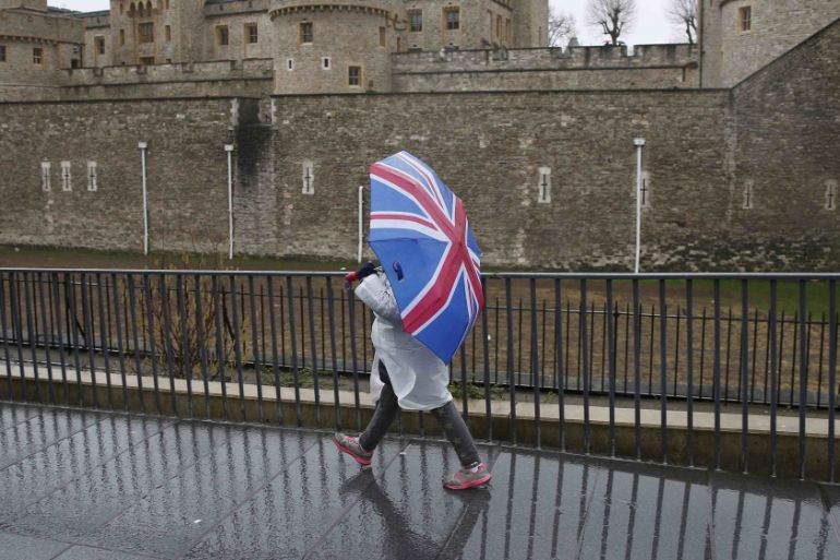 A tourist carrying a Union Flag umbrella walks in the rain during a spell of wet weather next to The Tower of London, in London