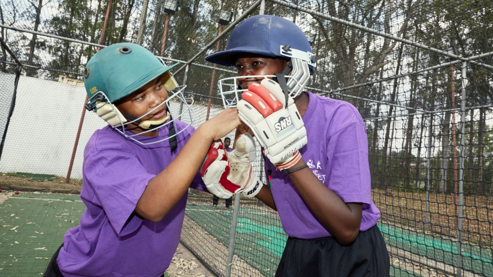 Vice Captain Mary Muvuka helps a teammate put her helmet on during a practice session at their training grounds at St Andrew's International School [Julia Gunther/Al Jazeera]