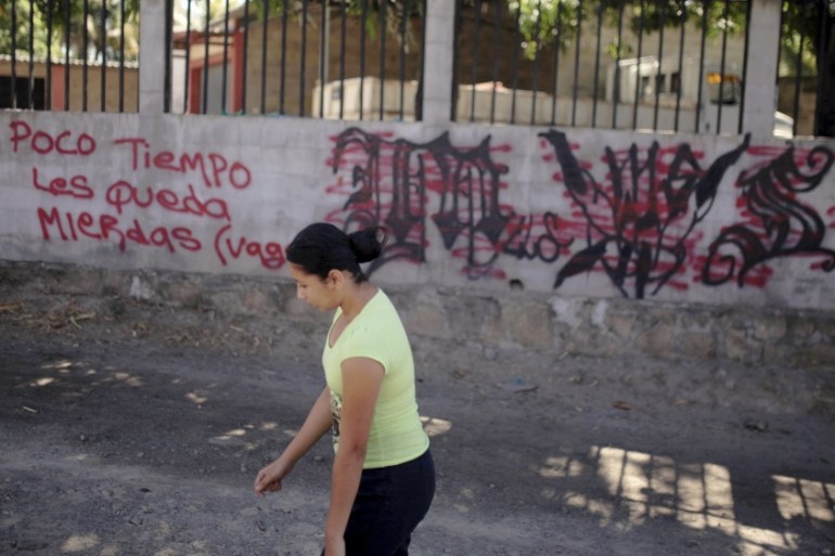 A woman passes by a message threatening gang rivals left on a wall next to MS-13 gang-related graffiti near a crime scene in San Luis Talpa, El Salvador