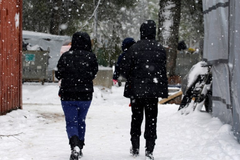 Stranded Syrian refugees carry their children through a snow storm at a refugee camp north of Athens