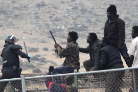 Migrants crossing a fence and facing policeman
