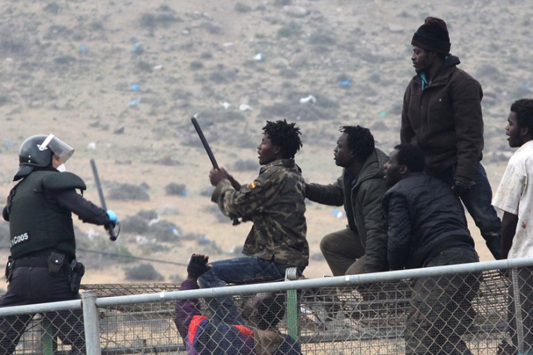 Migrants crossing a fence and facing policeman