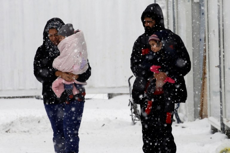 Stranded Syrian refugees carry their children through a snow storm at a refugee camp north of Athens