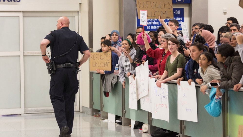 A police officer walks past people protesting against the travel ban at Dallas/Fort Worth International Airport [Laura Buckman/Reuters]