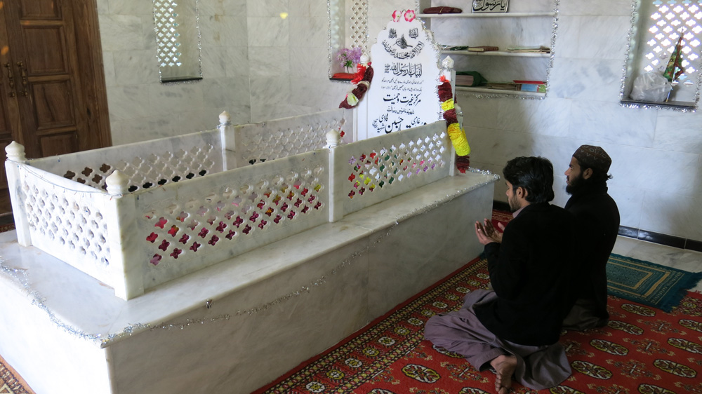 Two men pray beside the grave of Mumtaz Qadri [Asad Hashim/Al Jazeera]