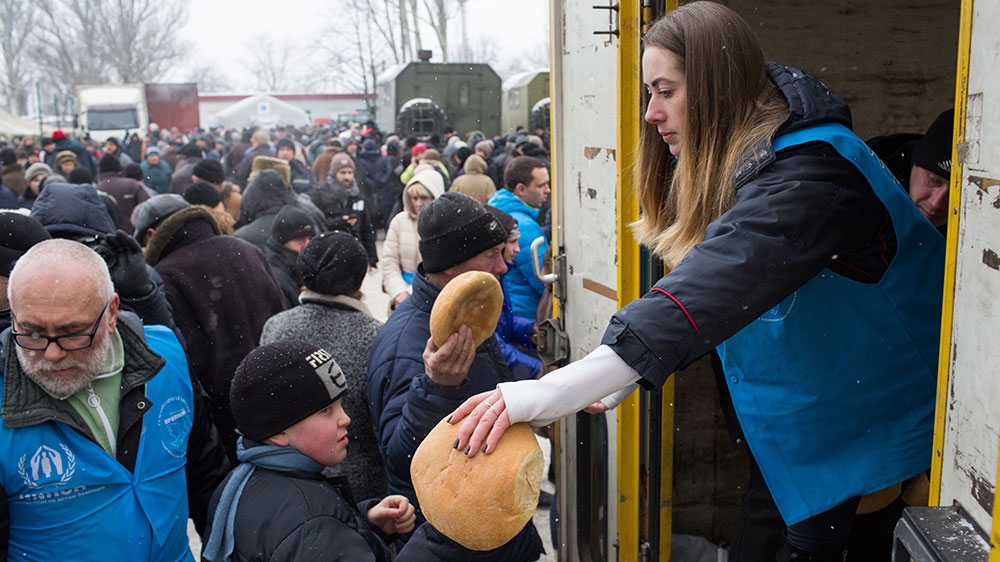 A volunteer hands out bread to people gathered at the central aid point in Avdiivka [John Wendle/Al Jazeera]