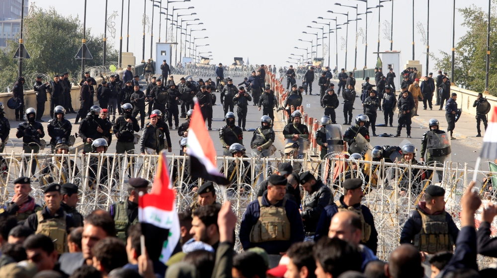 Riot police stand in front of demonstrators [Alaa Al-Marjani/Reuters]