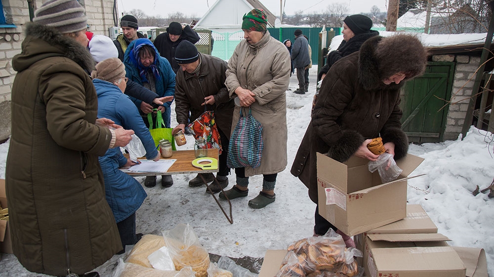 Pensioners gather at Nadezhda's house in Old Avdiivka to pick up donated supplies, such as biscuits, macaroni and cooking oil [John Wendle/Al Jazeera] 