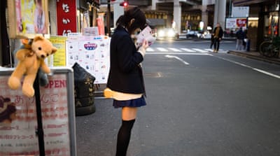 A uniformed girl stands outside a JK Cafe in Ikebukuro [Shiori Ito/Al Jazeera]