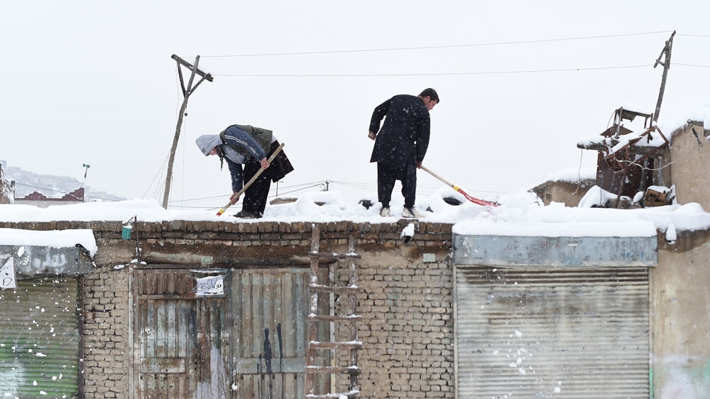 Afghan shopkeepers shovel snow from the roof of their shop during snowfall in Kabul [AFP]