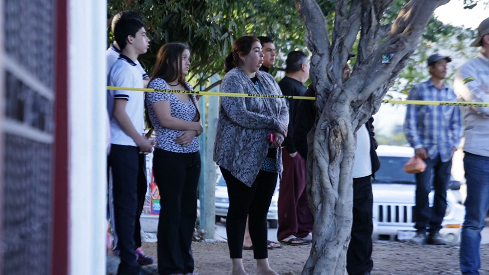 Residents of Villas del Real watch from behind the yellow tape after being woken up that morning by gunshots [Al Jazeera]