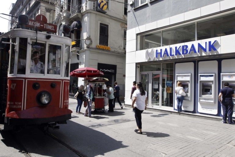 Customers use automated teller machines at a branch of Halkbank as a tram drives by in Istanbul