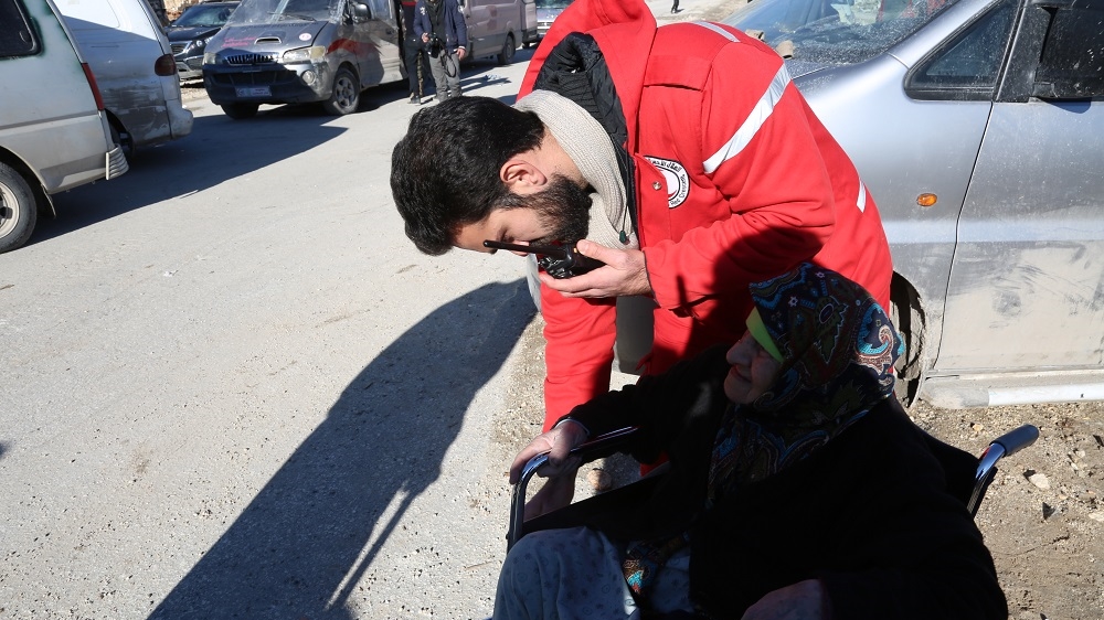 A Syrian Red Crescent member assists an elderly woman with her wheelchair [Malek Al Shimale/Al Jazeera]