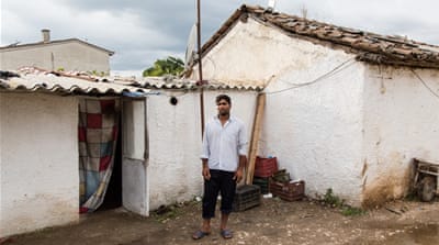 A migrant farm worker from Pakistan stands in front of the door to his home - a small room that sleeps 6 - in the village of Poullakida [Will Horner/Al Jazeera]