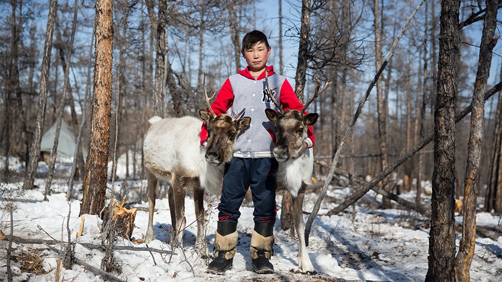A Dukha boy poses with two reindeer [Taylor Weidman/Al Jazeera]