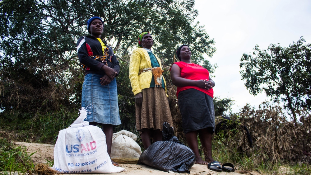 Siphiwenkosi Ndlovu, 20, Musa Ndlovu, 97 and Sehelo Msebele, 35 (left to right), wait to journey back across the river with their sacks of ground maize meal [Tendai Marima/Al Jazeera]
