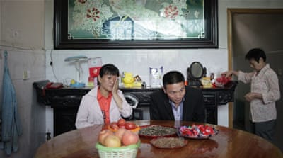 Cai Fengxia and her husband sit at the house of her birth parents. It is the first time Cai has met them since they abandoned her when she was 25 days old [Han Meng/Al Jazeera]