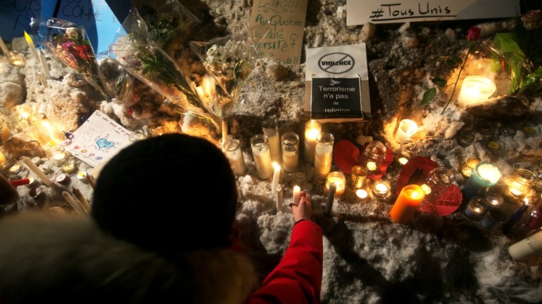 A woman places a candle at a memorial site near a sign saying "no violence" and "terrorism has no religion or identity" following a vigil Quebec mosque