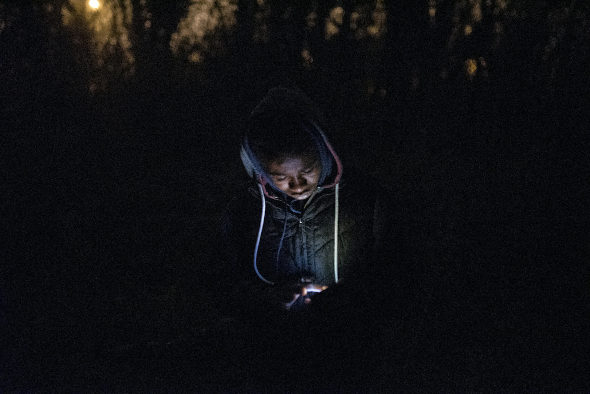 A young Sudanese man camping around the bunker in Calais uses his mobile phone in the pitch black [Guillem Trius/Al Jazeera]