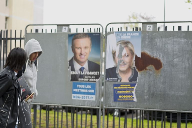 Youths walk past a defaced picture of Le Pen