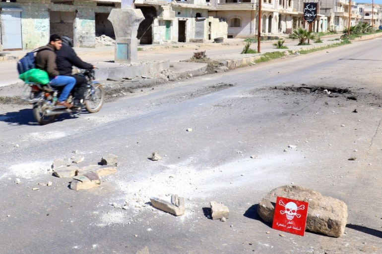 Men ride a motorbike past a hazard sign at a site hit by an airstrike on Tuesday in the town of Khan Sheikhoun in rebel-held Idlib