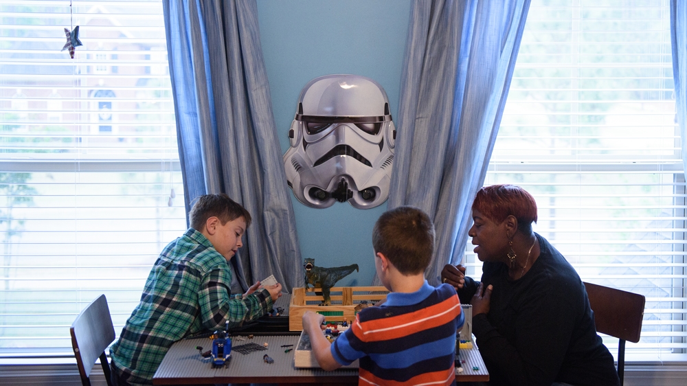 Robbie, left, and his best friend, Levi, play with Lego as respite caretaker Sharon Dyce watches [Andrew Craft/Al Jazeera]