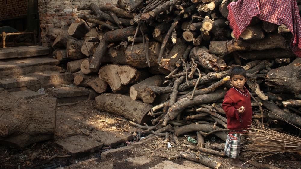 A Dom child stands near piles of wood. For Dom children, the cremation ground is their playground. They grow up watching scores of corpses burn in front of them every day and start to work there as children. [Radhika Iyengar/Al Jazeera]