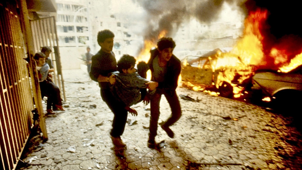 Civilian rescue workers evacuate the upper floor of a high-rise apartment building hit by artillery shells in Beirut in 1984 [George Azar/Al Jazeera]