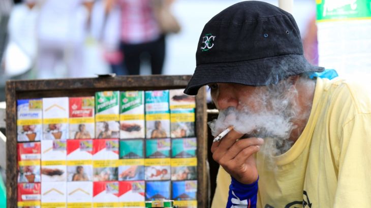 Vendor smokes beside his cigarette stall while waiting along a main street in Manila