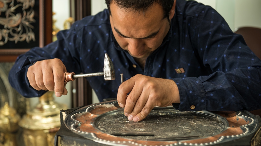 Craftsman Reza Galily works on a copper plate at a tourist shop in Isfahan [Wojtek Arciszewski/Al Jazeera] 