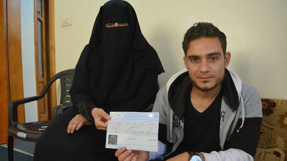 Walid's wife, Khadija, and son, Izzeldin, hold up Walid's one and only exit permit. He was unable to receive another one after refusing to collaborate with authorities [Mersiha Gadzo/Al Jazeera]